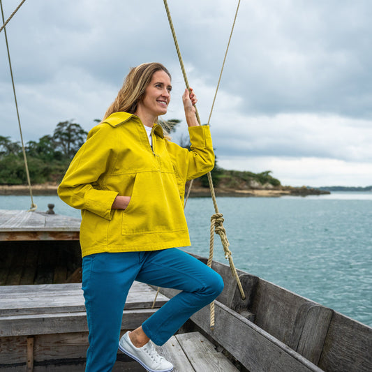 Image of a woman standing on a sailing boat wearing the Mosqueton Yelli Canvas Smock-style top in bright yellow.